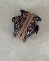 Zapatillas bajas de cuero vacuno con estampado animal print de leopardo, suela marrón y detalles en cuero negro.