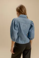 Camisa de denim con mangas abullonadas y cierre frontal con botones. Presenta un diseño de calce cómodo con estructura definida.