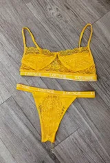 Conjunto de ropa interior de encaje amarillo, compuesto por un corpiño con breteles finos y una tanga con elástico con logo de la marca.