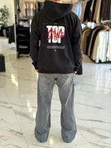 Canguro negro de corte oversize con capucha, manga larga y bolsillo tipo canguro al frente. En la espalda presenta un gran estampado gráfico con las palabras "Top Style" en blanco y rojo, acompañado de inscripciones y detalles minimalistas.
