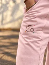 Pantalón jogger ancho color beige, con bolsillos laterales y pequeño bordado de un arco y flecha en la parte superior.