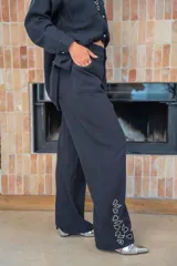 Pantalón blanco de tiro medio con botón y cremallera, detalles de strass en el bajo y corte amplio.