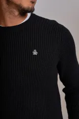 Sweater de punto con textura acanalada, color negro, de cuello redondo y manga larga. Presenta un pequeño logo bordado en el pecho.