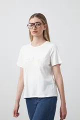 Remera blanca de manga corta, confeccionada en algodón, con bordado frontal en hilo color beige claro con la palabra "J'adore" en tipografía cursiva.