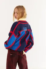 Sweater de punto con diseño geométrico en zigzag, combinando franjas en color marrón, rojo y negro. Presenta cuello redondo, mangas largas y un corte holgado.