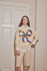 Sweater de lana color crudo, con diseño de moño grande estampado en el frente en tonos marrón, azul y rosado. Presenta cuello redondo, mangas largas con puños acanalados y corte holgado.