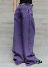 Jean de corte oversized y tiro medio-alto, confeccionado en denim de color violeta con diseño de cinco bolsillos y cierre frontal con botón y cremallera.