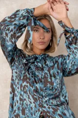 Camisa de seda con estampado animal print en tonos azules y marrones. Presenta cuello con lazo, cierre frontal con botones forrados y mangas largas con puños ajustables mediante lazos.