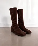 Bota de caña alta confeccionada en gamuza color marrón, con punta cuadrada, taco cuña corrido forrado y cierre lateral.