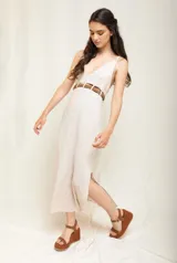 Vestido midi de lino imperial color beige, de tirantes anchos, escote en V y corte recto con tajo lateral. Incluye un cinturón de cuero trenzado con detalles metálicos.