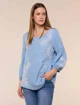Blusa de tencel celeste con escote cuadrado, mangas tres cuartos abullonadas con puños elastizados y delicados bordados florales blancos en el frente y las mangas.