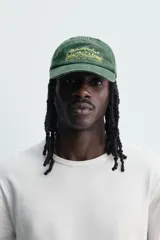 Gorra de siete paneles verde oscuro con efecto lavado, visera curva y bordado frontal en tono amarillo con la inscripción 'Bahia Montego'. Cuenta con ajuste posterior.