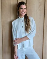 Camisa blanca de manga tres cuartos con cuello mao y botones oscuros en la vista frontal. Presenta costuras contrastantes en color claro.