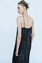 Vestido midi negro confeccionado en mezcla de viscosa con tejido satinado y efecto arrugado. Presenta escote en pico, tirantes finos ajustables, bajo con aplicación a tono y acabados deshilachados.