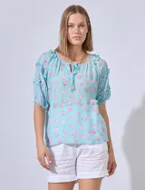 Blusa celeste con estampado floral, cuello redondo con lazo y mangas cortas con volados.