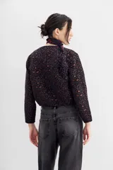 Campera bomber corta a la cintura con cuello redondo, confeccionada en jacquard con estampado de leopardo en tonos morados y marrones. Presenta una cartera frontal con cierre adornada con piedras y strass.