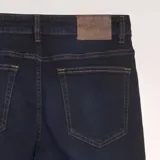 Pantalón de jean azul oscuro, corte slim, con bolsillos delanteros y traseros y costuras en color ocre.