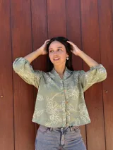 Camisa de corte holgado en color verde con estampado floral lineal en tono crema. Presenta cuello mao, cierre frontal con botones y mangas tres cuartos con puños elásticos.