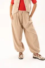 Pantalon tipo babucha de color beige, con silueta relajada y acabado suave tipo piel de durazno. Presenta cintura regulable con cordón y elástico en los tobillos que genera una forma abuchonada.