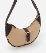 Cartera tipo baguette de diseño curvo, confeccionada en material sintético efecto gamuza color beige con detalles de costuras decorativas en los bordes y apliques en cuero sintético marrón. Cuenta con cierre superior, correa de hombro y herrajes metálicos en tono dorado claro.