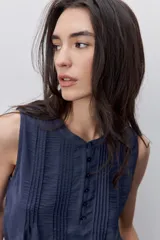 Blusa sin mangas color negro, de silueta fluida, con cuello redondo, detalle de alforzas en el frente y abotonadura parcial con botones visibles.