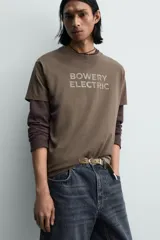 Camiseta de manga corta y cuello redondo, color marrón oscuro, con estampado frontal que dice "BOWERY ELECTRIC" en tipografía desgastada.