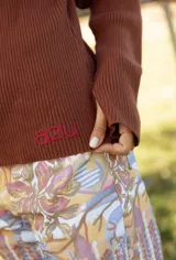 Polera de tejido de punto acanalado color chocolate, con cuello alto y mangas largas. Presenta un pequeño bordado en el ruedo inferior.