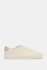 Zapatilla urbana color off-white con detalle trasero en contraste de tono tostado y suela engomada. Presenta pespuntes decorativos en el cuerpo y cierre de cordones.