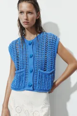 Chaleco azul de punto calado con cuello redondo, sin mangas, cierre frontal con botones y dos bolsillos de parche en la parte delantera.