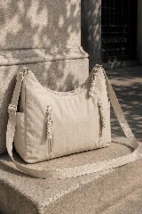 Cartera hobo gris de tela suave y liviana, con bolsillos frontales con cierre y tiradores trenzados, correa ajustable y compartimento principal con cierre.
