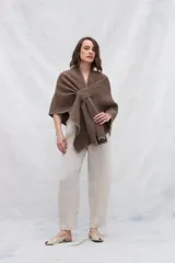 Ruana de tejido de punto industrial en color marrón, confeccionada en lana fina sin teñir. Presenta un diseño con doble ojal que permite mantener la prenda cruzada y cerrada.