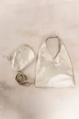 Bolso de hombro color beige, confeccionado en cuero sintético con interior plateado. Presenta un bolsillo externo con cierre.