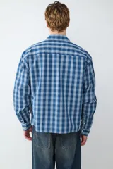 Camisa de mangas largas color azul con estampado a cuadros blancos, de corte boxy. Presenta cierre frontal con botones, cuello con solapa y un bolsillo en el pecho.