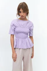 Remera blanca de algodón con cuello redondo, mangas cortas y detalle de fruncido tipo nido de abeja en la zona del busto, creando un efecto peplum.