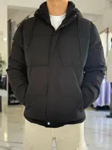 Campera puffer impermeable color beige con capucha desmontable con cordones negros, cierre frontal con cremallera y solapa con botones a presión.
