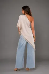 Blusa de un hombro en color marfil, confeccionada en tejido fluido con diseño asimétrico y terminaciones con puntilla en el borde y la manga.