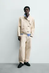 Cazadora de algodón color beige claro, corte relajado, con cuello subido y manga larga. Cierre frontal con cremallera oculta por solapa con cierres metálicos tipo alamar.