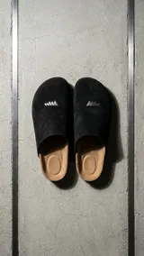 Zueco estilo sandalia de diseño cerrado, color beige, confeccionado en material texturizado con plantilla anatómica y suela plana. Presenta el logotipo de la marca grabado en la parte frontal.