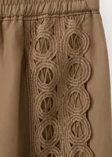 Pantalón marrón de corte recto, con cintura ajustable elastizada y cordón, y detalle de franja lateral bordada con diseño calado.