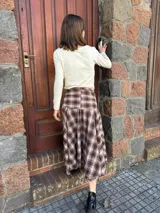 Pollera midi de corte amplio con estampado escocés en tonos marrones. Presenta un diseño distintivo con un detalle de atado en la cintura que simula puños de camisa y cierre frontal con botones.