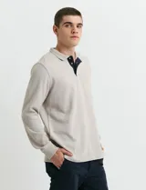 Remera de manga larga con cuello polo, confeccionada en tejido de punto canalé francés. Presenta abotonadura frontal con botones de madera y detalles a contratono en la cartera y el interior del cuello.