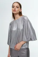 Blusa de corte holgado en color plateado metalizado, con cuello redondo y mangas amplias tipo murciélago.
