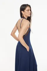 Vestido largo azul marino, de corte fluido, con escote halter, detalles trenzados en los hombros, bolsillos laterales y tajo profundo en la pierna.