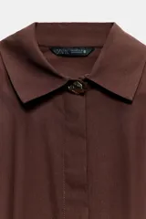 Camisa de cuello solapa y manga larga, confeccionada en popelín. Presenta un diseño con cintura entallada mediante pliegues y cierre frontal con botones ocultos por solapa.