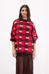 Sweater de punto con diseño geométrico de cuadros en tonos bordó, rojo y rosa. Presenta cuello redondo, mangas largas con puños ajustados y un corte holgado.