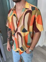 Camisa de manga corta con cuello cubano, confeccionada en fibrana con un estampado abstracto de formas geométricas en tonos naranja, marrón, verde y beige.