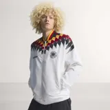 Campera deportiva Adidas de la selección de Alemania, inspirada en el diseño de 1994. Es de color blanco con un estampado geométrico en los hombros que combina los colores de la bandera alemana (negro, rojo y amarillo). Presenta cierre frontal, cuello redondo y el logo de la marca junto al escudo de la DFB en el pecho.