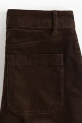 Pantalón de pana de algodón color marrón oscuro, de tiro alto, con piernas acampanadas y bolsillos parche delanteros y traseros.