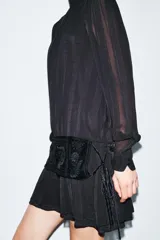 Vestido corto de viscosa color negro con cuello perkins y manga larga. Presenta un fajín de terciopelo integrado con bordados a tono y detalle de lazadas laterales.
