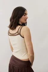Musculosa de tejido rib color beige con detalles en marrón oscuro en el escote y doble tirante fino. Presenta un pequeño texto estampado en el pecho.
